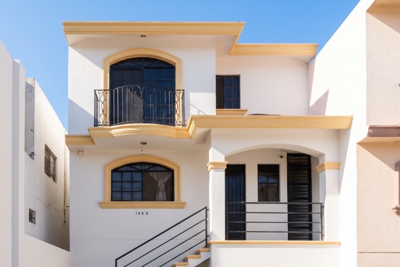 Fachada de casa de dos pisos recién pintada en blanco con molduras color arena y herrería en negro